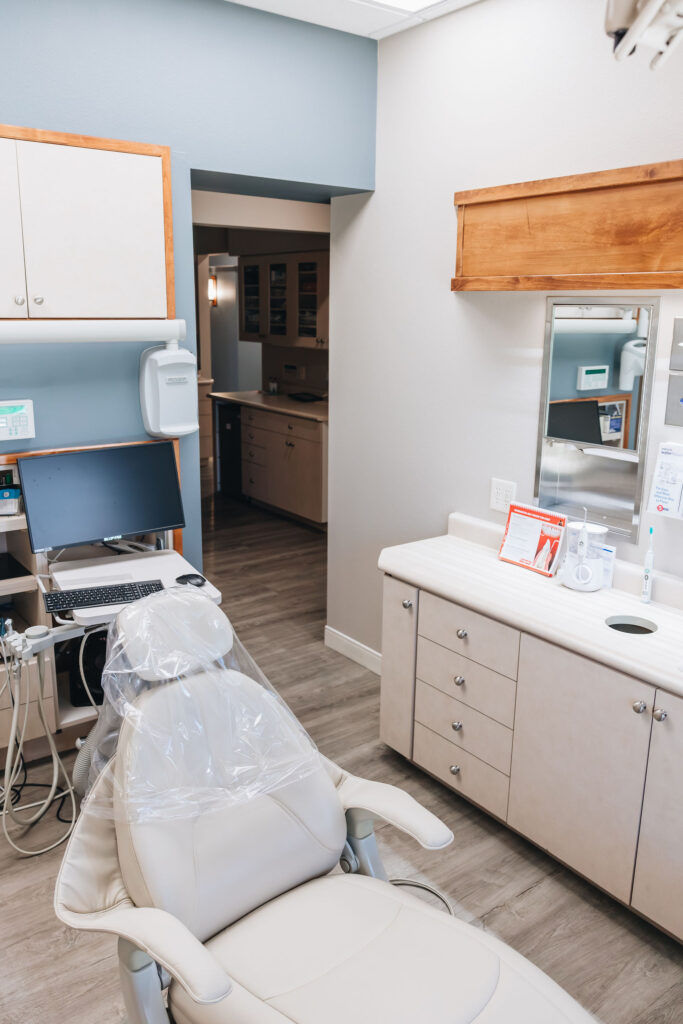 A dentist office with a chair, computer, counter, and blue wall.