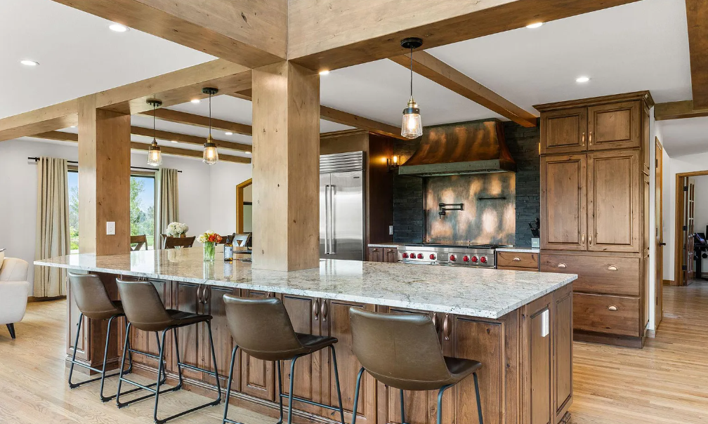 An interior kitchen with wood accents, cabinets, and floors, with a marble countertop and brown leather high chairs.